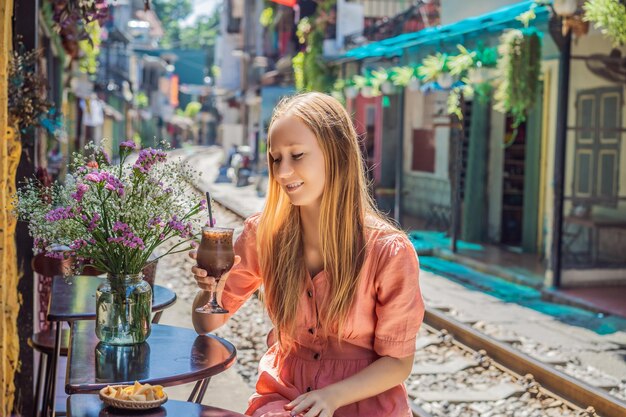 Young woman traveler drinks coffee sitting by the railway paths which go through residential area in