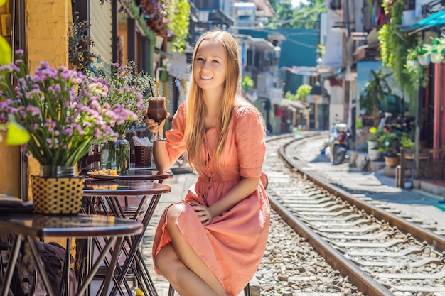 Young woman traveler drinks coffee sitting by the railway paths which go through residential area in