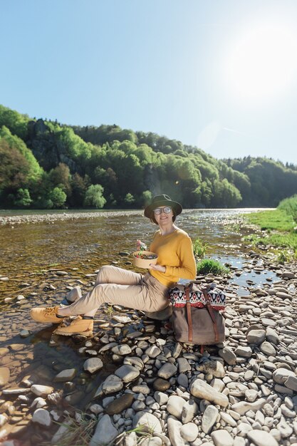 Young woman traveler eat healthy food near river on nature background