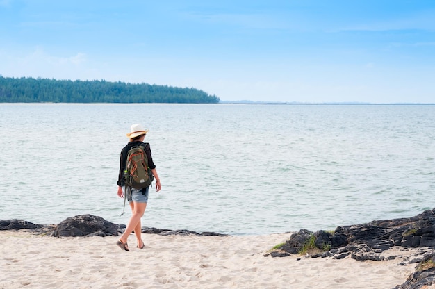 Young woman traveler put the hat with rucksack backpacks on sea beach enters the sea