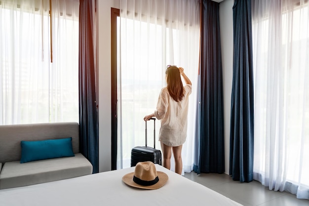 Young woman traveler with luggage looking at view in hotel room on summer vacation