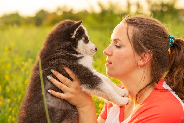 Young woman in a Tshirt hugs a husky puppy at sunset outdoors