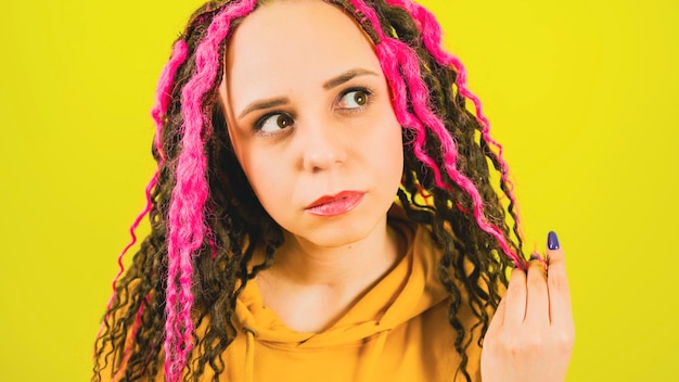 Young woman twists hair with thoughtful look on yellow background Beautiful female with curly hair looking away and reflecting on life