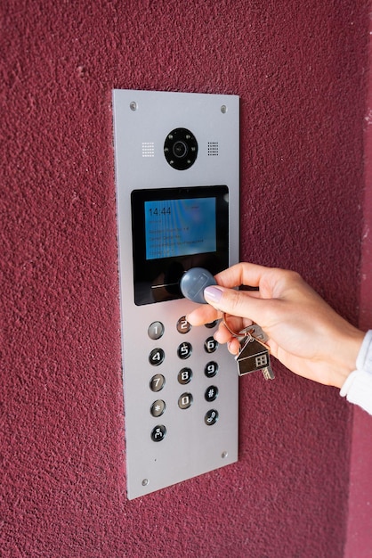 A young woman types the apartment code on the electronic intercom panel opens the door with a touch key the screen for viewing information Protection and security concept