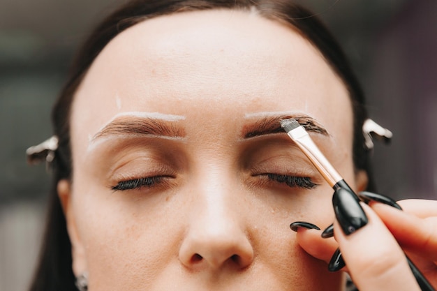 A young woman undergoes an eyebrow correction procedure in a beauty salon closeup the girl paints her eyebrows in the salon