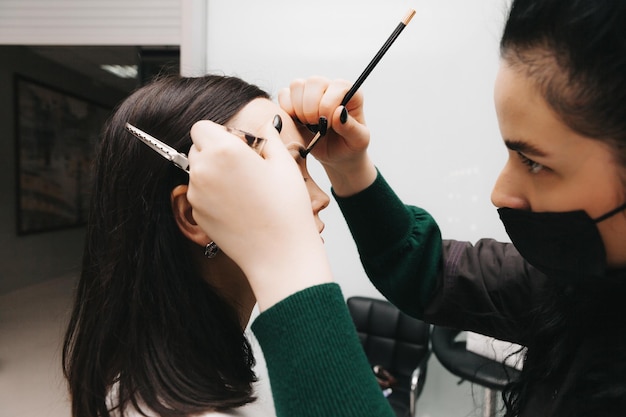 A young woman undergoes an eyebrow correction procedure in a beauty salon closeup the girl paints her eyebrows in the salon