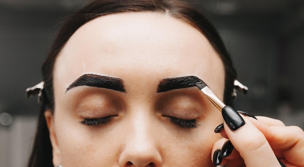 A young woman undergoes an eyebrow correction procedure in a beauty salon closeup the girl paints her eyebrows in the salon