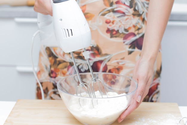 Young woman uses mixer in beating eggs, stands in a modern kitchen