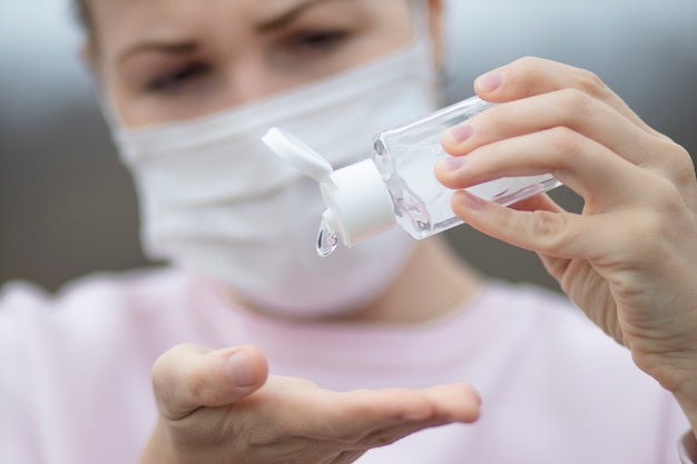 Young woman using, applying sanitizer from portable bottle for disinfect hands, girl in protective mask on face. Disinfection, disinfecting hands against coronavirus, virus bacteria. Pandemic covid-19