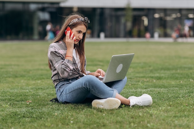 Young woman using computer on green grasses in the park. freelance working outdoor or relaxation concept