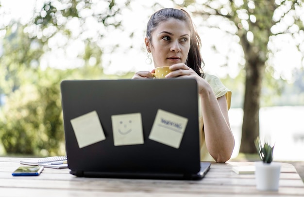 Young woman using laptop computer in the public park Millennial female freelancer working remotely and taking notes in a city park Technology and remote work concept Using tech devices outdoors