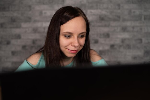 Young woman using laptop computer sitting in front of white brick wall background people and technology lifestyles education business concept