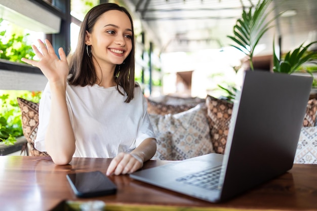 Young woman using laptop and making video call in cafe.