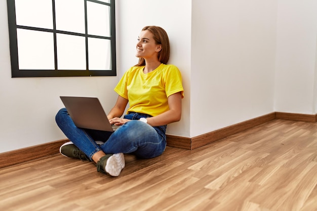 Young woman using laptop sitting on floor at empty room