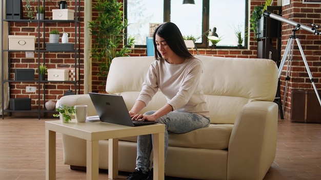 Young woman using laptop while sitting on sofa at home