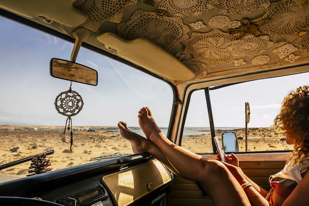 Young woman using mobile phone leaning in car with legs on dashboard. Woman text messaging mobile phone. Enjoying road trip. Female tourist sitting in car using phone while resting feet on dashboard