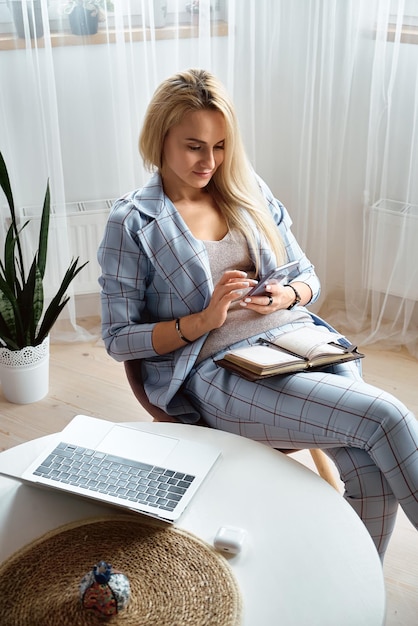 Young woman using mobile phone sitting at home office desk remote work at home