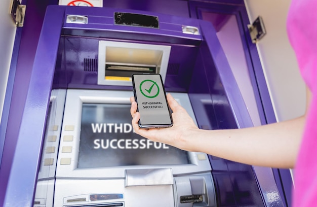 Young woman using the smart phone for cardless withdrawing the cash near the atm