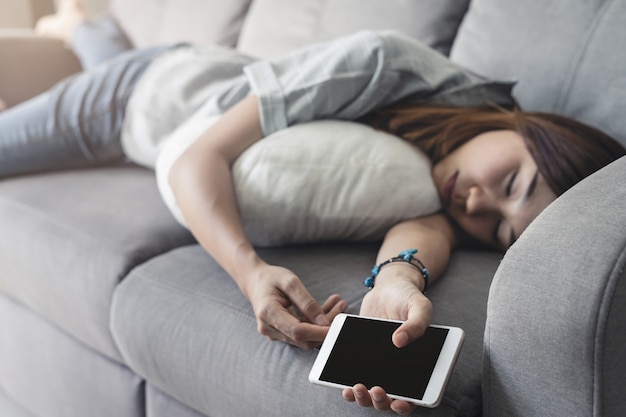 Young woman using smartphone at cozy home and sleeping on sofa in living room