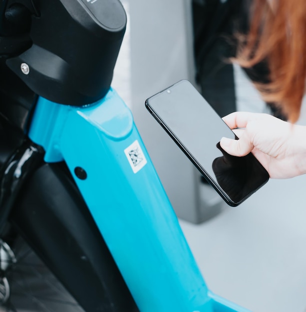 Young woman using smartphone hands using smartphone scanning the QR code of shared bike in city and looking on display unlocking city rental bike stand Female renting bike using rental app on phone