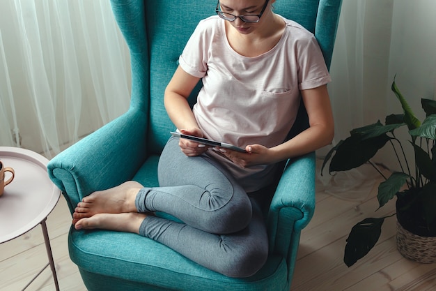 Young woman using a tablet while sitting in a comfortable chair