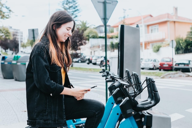 Young woman using using a rental bike stand city system super happy smiling while testing the bikesEuropean city with a rental bike green transport