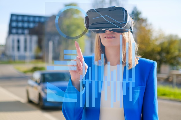 Young woman using virtual reality goggles to analyze data and graphics in colorful neon lights futur