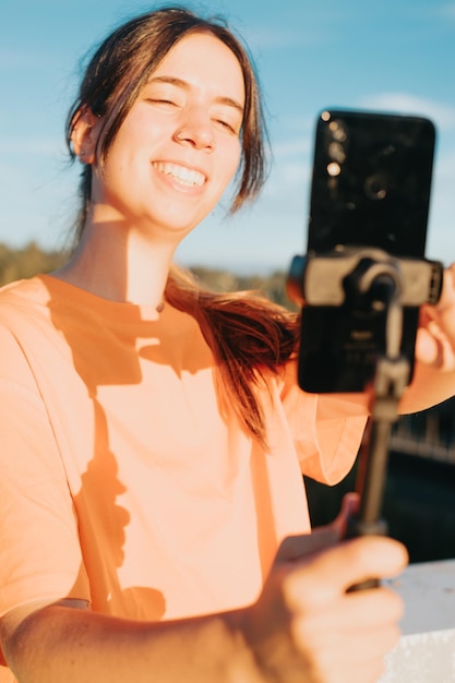 Young woman video blogger with a smile on her face takes videos of herself on the phone while broadcasting on an urban space while training sport influencer recording clip of herself with smartphone