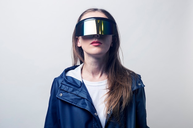 Young woman in virtual reality glasses in a blue jacket on a light background.