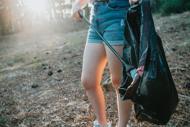 Young woman volunteer cleaning up the forest and collecting trash into a bag Sustainability save the planet Nature cleaning ecology green conceptEnvironment plastic pollution with copy space