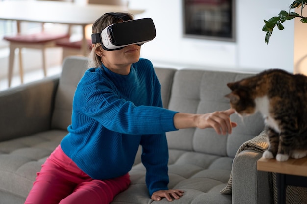 Young woman in VR glasses explores game and tries to touch domestic cat sitting on wooden table