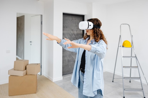 Photo young woman in vr glasses using modern technology creating room design moving hands in air standing in new apartment during renovation virtual reality and repair concept