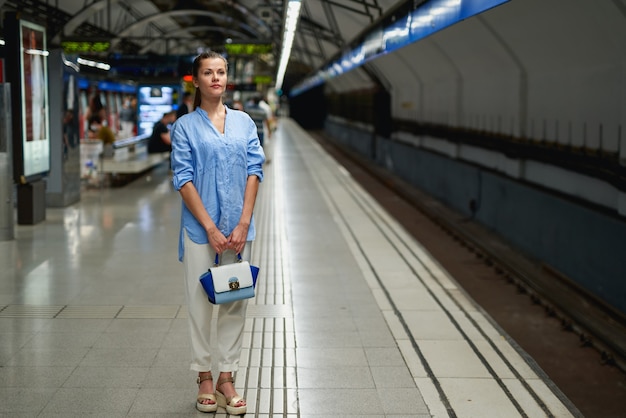 Young woman waiting on the platform of a railway station for train to arrive. Public transport.