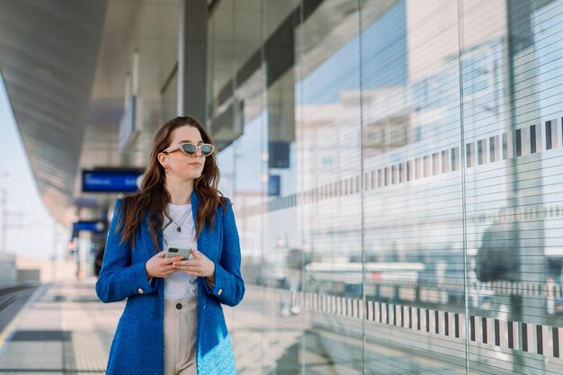 Young woman waiting at rail station Holding smartphone and waiting for her train Public transport