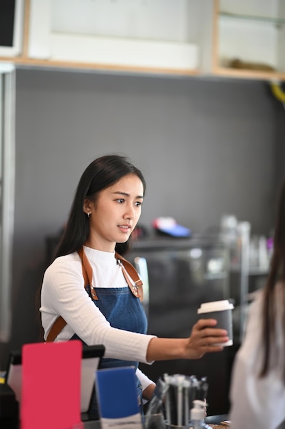 Young woman waitress serving cup of coffee to customer in coffee shop.