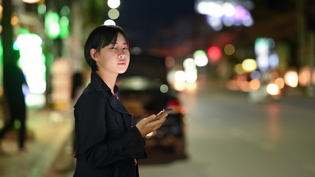 A young woman waits for her private taxi while using a transportation app on mobile