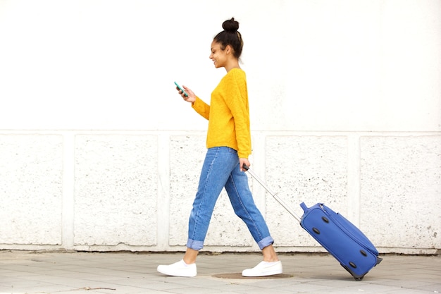 Photo young woman walking with travel bag and using mobile phone