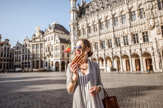 Photo young woman walking with waffle a traditional belgian pastry food in the center of brussels city during the morning