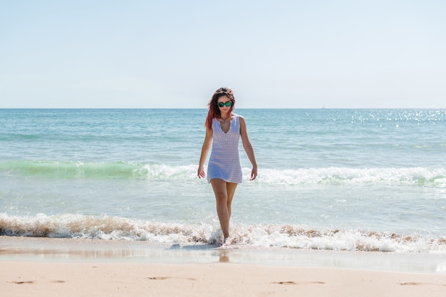 Young woman walks on the beach in a white dress