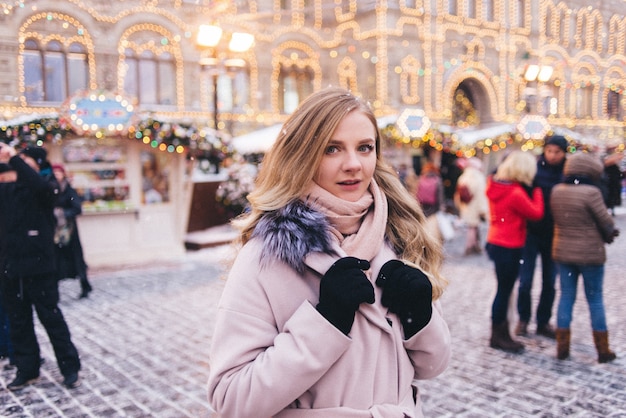 Photo a young woman walks at christmas in the square near the decorated christmas trees. candy is a lollipop in the form of a heart.