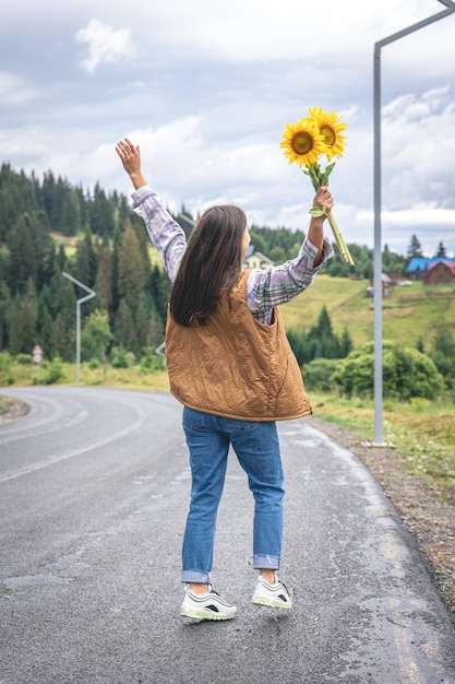 A young woman walks in the mountains with a bouquet of sunflowers