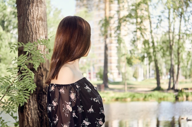 Young woman walks in the park and looks at city buildings in the distance