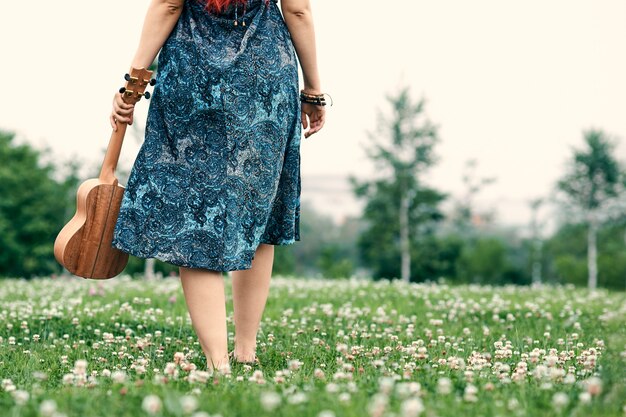 Young woman walks through a summer glade holding a ukulele in her hand.