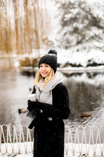 Young woman in warm clothes enjoying in snow with takeaway coffee cup