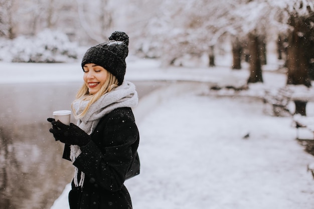 Young woman in warm clothes enjoying in snow with takeaway coffee cup