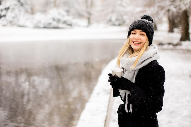 Young woman in warm clothes enjoying in snow with takeaway coffee cup