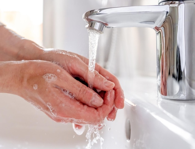 Young woman washes her hands with soap over the sink