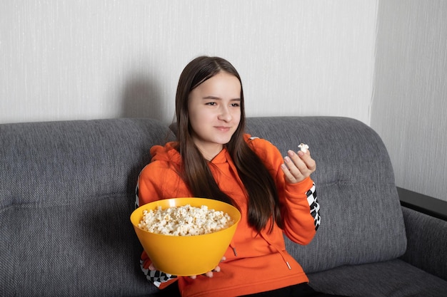 Young woman watching a funny show on tv with popcorn in her hands smiling