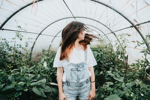 Young woman waving hair standing in greenhouse near plants with vegetables Sustainability and responsible growing concept Eco and bio healthy food harvesting