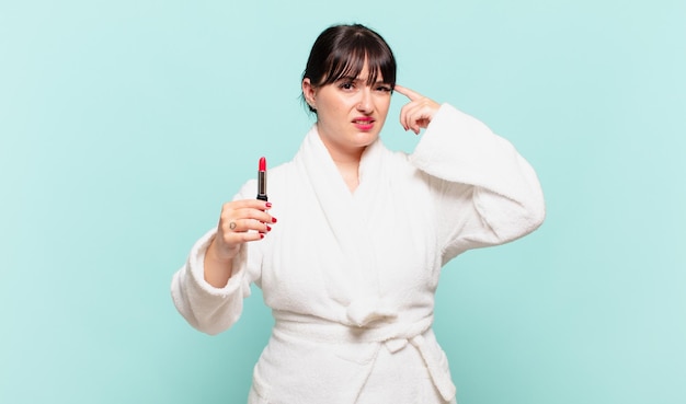 Young woman wearing bathrobe feeling confused and puzzled showing you are insane crazy or out of your mind